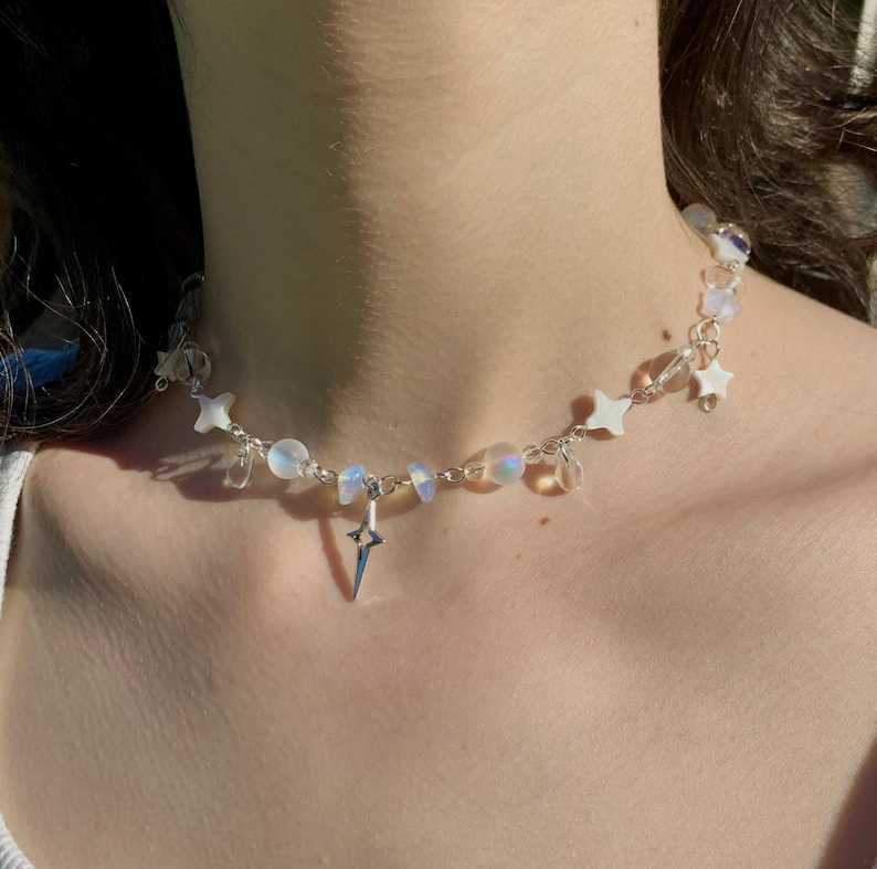 May include: A silver necklace with iridescent white beads and star charms. The necklace has a silver lightning bolt pendant.