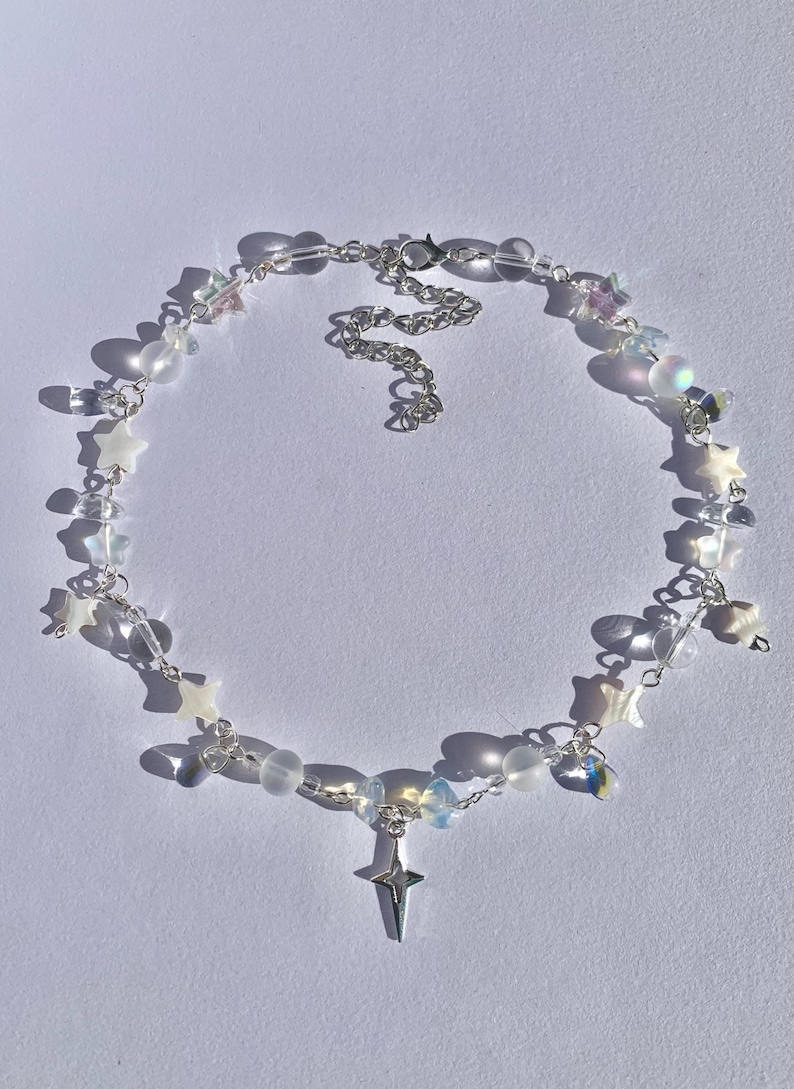 May include: A delicate silver chain necklace with a star charm and iridescent beads. The necklace features a variety of star-shaped charms and clear and opaque beads.