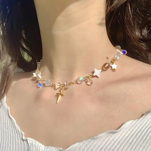 May include: A delicate gold necklace with a star charm and iridescent beads. The necklace is made of a thin gold chain and features a variety of small, clear beads and white star charms.