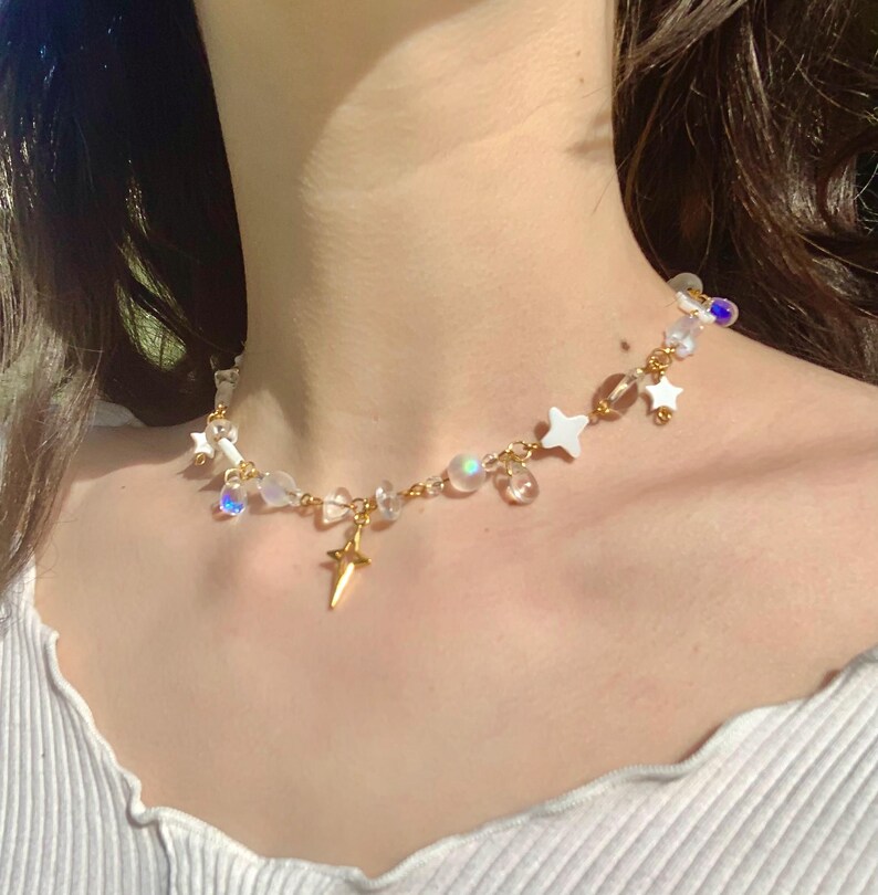 May include: A delicate gold necklace with a star charm and iridescent beads. The necklace is made of a thin gold chain and features a variety of small, clear beads and white star charms.
