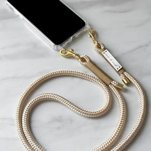 Chaîne pour téléphone portable beige/or avec mousqueton doré et emballage doré avec étui pour téléphone portable assorti avec œillets