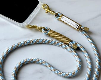 May include: A blue and beige braided phone strap with gold hardware and a small brass tag that reads "moon & rebel".