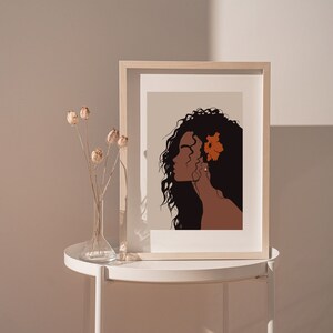 May include: A framed illustration of a woman with long, dark hair and a single orange flower behind her ear. The background is a light beige color.