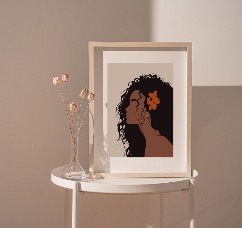 May include: A framed illustration of a woman with long, dark hair and a single orange flower behind her ear. The background is a light beige color.