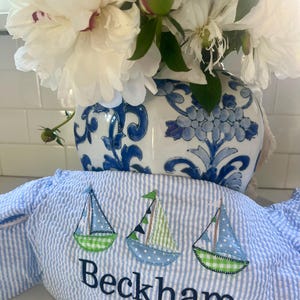May include: A blue and white striped fabric with three embroidered sailboats and the name "Beckham" in black embroidery.