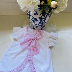 May include: White hooded towel robe with pink gingham trim and a pink bow. The robe has the monogram "Miss" embroidered on the front.