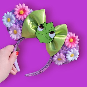 May include: Purple and green sequined headband with a green chameleon character and pink and white flowers.