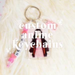 May include: Custom anime keychain featuring a character illustration. The keychain has a clear acrylic base with a silver keyring. The text "custom anime keychains" is displayed in white. A pink beaded charm is attached.