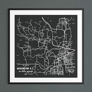 May include: A framed map print featuring a dark grey background with white lines depicting roads and locations. The text reads: The City of WASHINGTON D.C. THE CAPITAL WASTELAND 2277. The print is enclosed in a thin black frame with a white mat border.