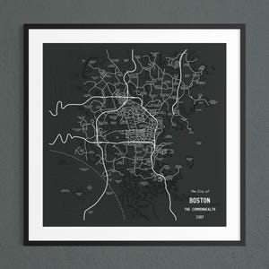 May include: A framed map print featuring a dark gray background with white lines depicting roads and geographical contours. The text reads The City of BOSTON THE COMMONWEALTH 2287. The design includes various labeled locations across the map area.