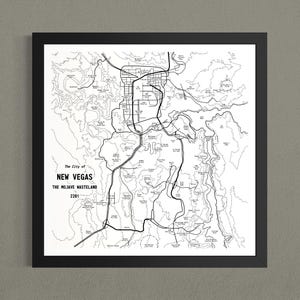May include: A framed black and white map print titled The City of NEW VEGAS THE MOJAVE WASTELAND 2281. The artwork features thin black lines depicting roads, topographical contours, and various landmarks on a stark white background within a black frame.