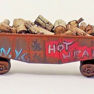 May include: A rusty red toy train car filled with wooden logs. The car has graffiti that says "N.Y.C." and "HOT HEAD".