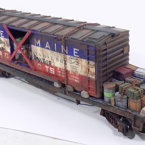 May include: A detailed model train car with a weathered appearance. The car is painted in red, white, and blue with the words "STATE" and "MAINE" visible. It is loaded with barrels, crates, and other cargo, and has the text "DANGER" on the side.