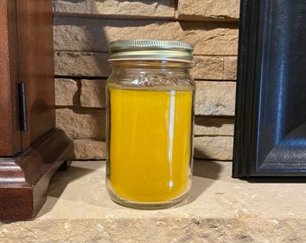 May include: A yellow candle in a clear glass jar with a gold lid. The jar has the word "MASON" printed on it. The candle is sitting on a stone surface.