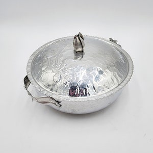 May include: Silver aluminum serving dish with a floral design and a lid. The dish has two handles and a knob on the lid.