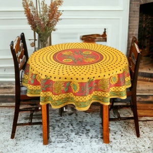 May include: A round yellow tablecloth with a red and green border featuring a sunflower design. The tablecloth is laid on a round wooden table with two wooden chairs.