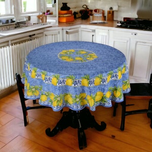 May include: A round blue tablecloth with a white border and a lemon print. The tablecloth is on a round table with a black base. Two black chairs are visible in the background.