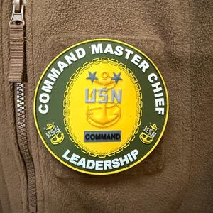 May include: A yellow and green round patch with the words "Command Master Chief" and "Leadership" around the edge. The center of the patch features a gold anchor with two stars above it and the letters "USN" below it. The words "Command" are printed in black on a yellow background.