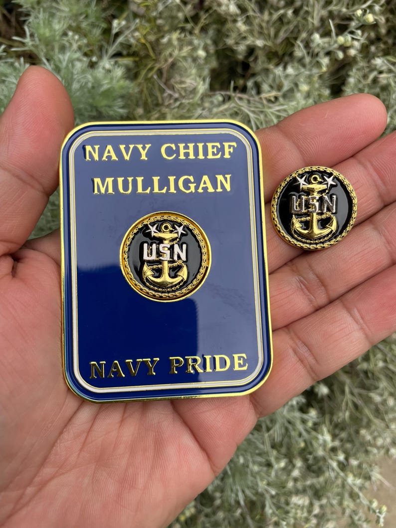 K&ouml;nnte beinhalten: Eine goldfarbene Metallplakette mit blauem Hintergrund und goldener Beschriftung. Die Plakette tr&auml;gt die Aufschrift "Navy Chief Mulligan Navy Pride". Au&szlig;erdem ist eine goldfarbene Metallnadel mit schwarzem Hintergrund und goldener Beschriftung zu sehen. Die Nadel tr&auml;gt die Aufschrift "USN".