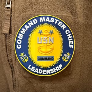 May include: A blue and yellow embroidered patch with the words "Command Master Chief" and "Leadership" around a circle containing a gold anchor, two stars, and the letters "USN". The patch also has a smaller gold rectangle with the word "Command" inside.
