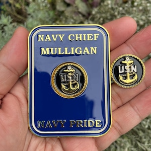 K&ouml;nnte beinhalten: Eine goldfarbene Metallnadel mit blauem Hintergrund und einem goldenen Anker mit den Buchstaben USN in Wei&szlig;. Die Nadel befindet sich neben einer gr&ouml;&szlig;eren goldfarbenen Metallplakette mit blauem Hintergrund und dem Text "NAVY CHIEF MULLIGAN" und "NAVY PRIDE".