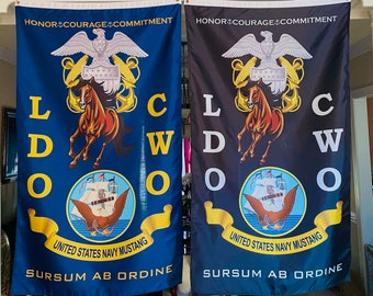 Puede incluir: Dos banderas azul marino y negras con las palabras "HONOR COURAGE COMMITMENT" y "LCWO" impresas en ellas. Las banderas también presentan un águila dorada con un escudo rojo, blanco y azul, un caballo rojo y un barco con un águila blanca en la parte superior. El texto "UNITED STATES NAVY MUSTANG" y "SURSUM AB ORDINE" está impreso en las banderas.
