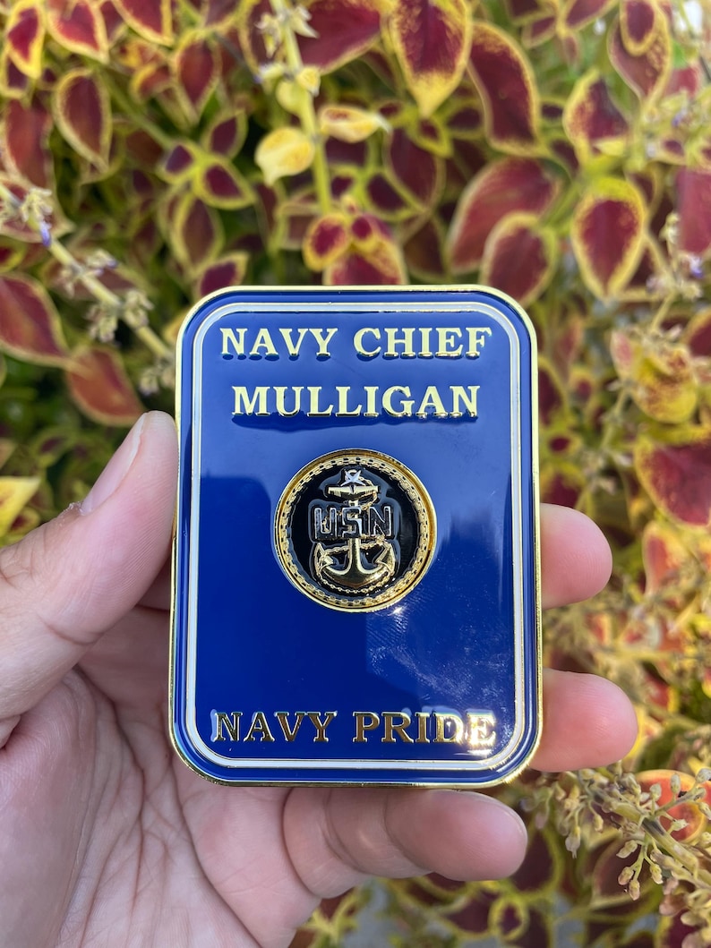 K&ouml;nnte beinhalten: Eine goldfarbene Challenge-M&uuml;nze mit blauem Hintergrund. Die M&uuml;nze zeigt den Text "NAVY CHIEF MULLIGAN" und "NAVY PRIDE" in wei&szlig;en Buchstaben. Ein goldfarbener Anker mit den Buchstaben "USN" befindet sich in der Mitte der M&uuml;nze.