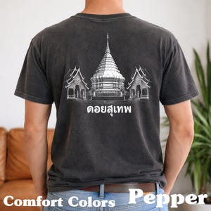 Peut inclure: T-shirt gris foncé avec un motif blanc d'un temple et le texte "ดอยสุเทพ". Le t-shirt est fabriqué en tissu Comfort Colors.