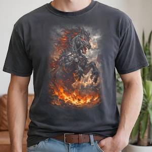 Könnte beinhalten: Dunkelgraues T-Shirt mit einer detaillierten Illustration eines schwarzen Pferdes mit feuerroter Mähne und Augen, das sich inmitten von Flammen aufbäumt. Das Kunstwerk zeigt eine Kampfszene mit einem stürmischen Himmel im Hintergrund.