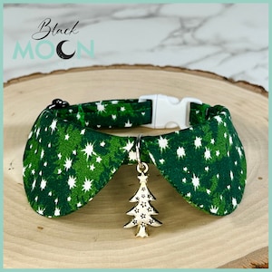 May include: A green fabric pet collar featuring a white star pattern and a white plastic side-release buckle. A silver-toned metal charm shaped like a Christmas tree with star cutouts hangs from a metal D-ring attached to the collar band.