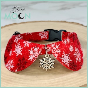 May include: A red pet collar featuring a white snowflake pattern and a silver-toned metal snowflake charm. The collar includes a black plastic side-release buckle and an adjustable slider. The text Black MOON CRAFT is visible in the background.