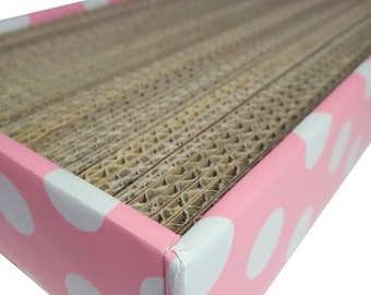 May include: Pink cardboard scratching post for cats with white polka dots. The scratching surface is made of corrugated cardboard.