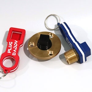 Peut inclure: Un ensemble de trois porte-clés avec un bouchon en laiton, un porte-clés bleu et blanc avec le texte "PLUG" et un porte-clés rouge avec le texte "DACVA PLUG".