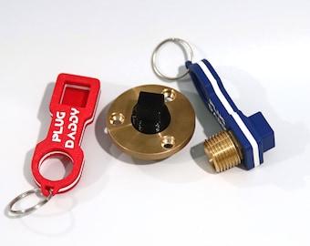 May include: A set of three keychains with a brass plug, a blue and white keychain with the text "PLUG" and a red keychain with the text "DACVA PLUG".