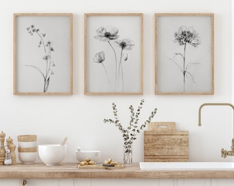 May include: Three black and white line drawings of flowers in simple wooden frames hang on a white wall above a wooden countertop with a white porcelain sink and gold faucet.