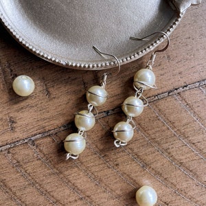 May include: A pair of pearl earrings with a silver wire design. The earrings are hanging from a silver tray.