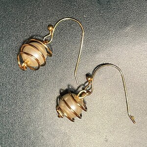 May include: A pair of gold earrings with a pearl-like bead encased in a wire cage.
