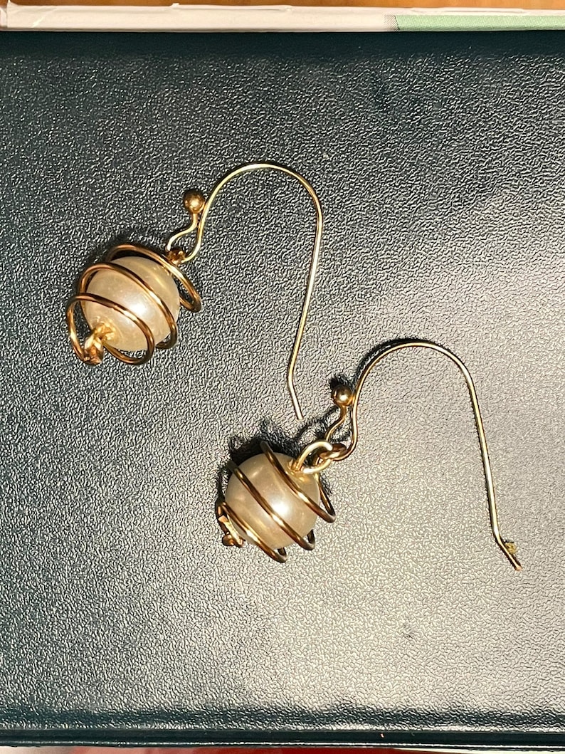 May include: A pair of gold earrings with a pearl-like bead encased in a wire cage.