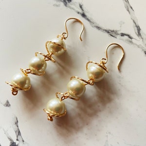 May include: A pair of gold earrings with white pearl beads wrapped in a spiral design.