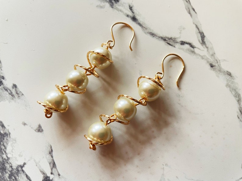 May include: A pair of gold earrings with white pearl beads wrapped in a spiral design.