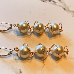 May include: A pair of gold earrings with three white pearls each, wrapped in gold wire.