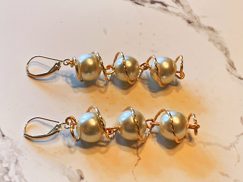 May include: A pair of gold earrings with three white pearls each, wrapped in gold wire.