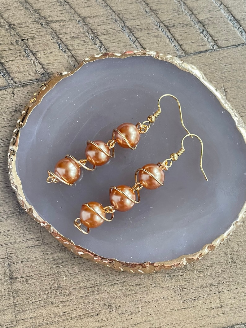 May include: A pair of gold-toned earrings with a spiral design and brown pearl accents.