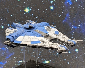 Op de afbeelding: Een miniatuur ruimteschipmodel, voornamelijk blauw en wit, met gedetailleerde panelen en wapens. Het model staat tegen een achtergrond van een sterrenstelsel, wat duidt op een verzamelobject of spelonderdeel met ruimtethema.