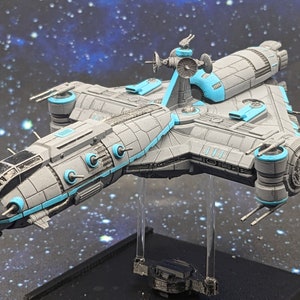 May include: A detailed model of a spaceship, primarily gray with light blue accents. The spaceship has multiple turrets, engines, and a central tower. It is mounted on a clear stand against a starry background, suggesting a space theme.