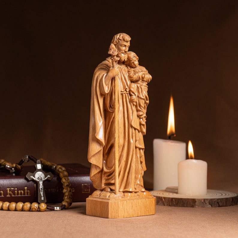 May include: A wooden statue of Saint Christopher carrying a child on his shoulder. The statue is standing on a wooden base and is surrounded by candles.