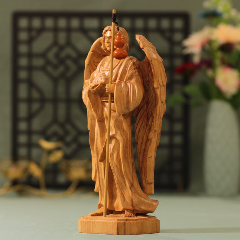 May include: A wooden sculpture of an angel with wings outstretched, holding a staff with gourds hanging from it. The angel is carved in a light brown wood and has a serene expression.
