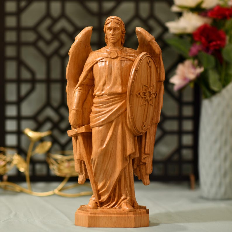 May include: A wooden sculpture of an angel with wings outstretched, holding a sword and shield. The angel is carved in a realistic style and has a serene expression.