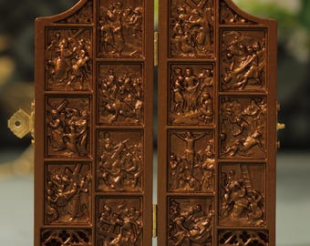 May include: A brown, hinged diptych with detailed relief carvings depicting religious scenes. The panels are divided into rectangular sections, each showcasing a different biblical narrative. A small, gold-colored latch secures the diptych.