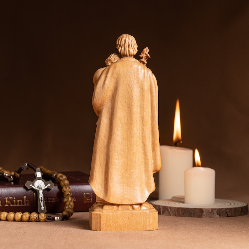 May include: A wooden statue of Saint Joseph holding a child. The statue is carved from light wood and has a natural finish. The statue is standing on a wooden base.